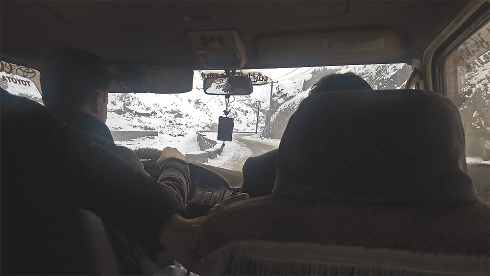 View out the front windshield of a snowy road from inside of a car