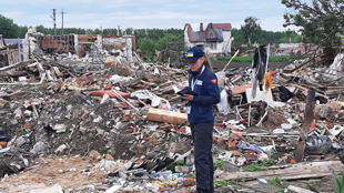A woman stands near piles of debris and looks down at a booklet.