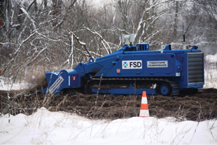 A blue, tracked machine drives through the mud and snow.