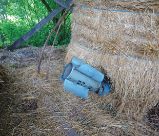 The tail end of a rocket sticks out of a bale of hay.