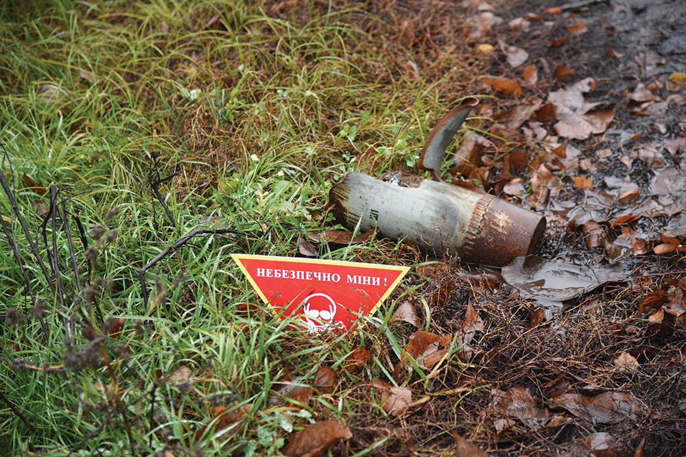 A rusty piece of metal and a red warning sign lie side-by-side in the grass.