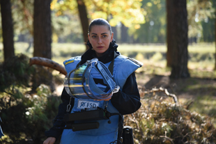 A woman wearing personal protective gear holds a polycarbonate visor.