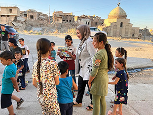 A woman walks along a street with children holding a handout.