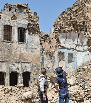 Two people pointing upward a ruined building.