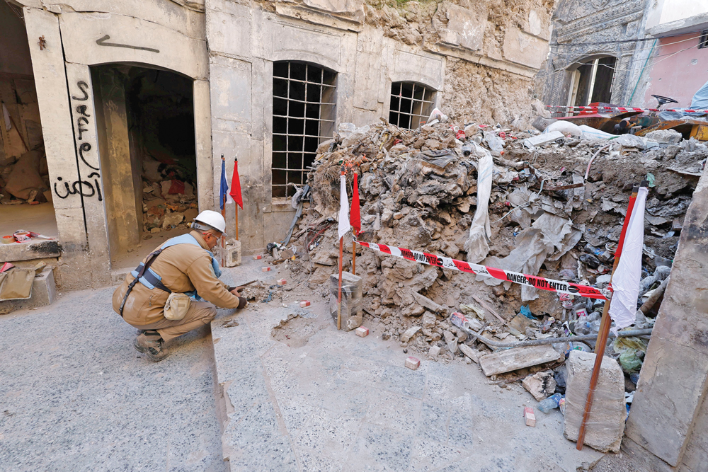 A man kneeling down beside a large pile of rubble behind red tape.