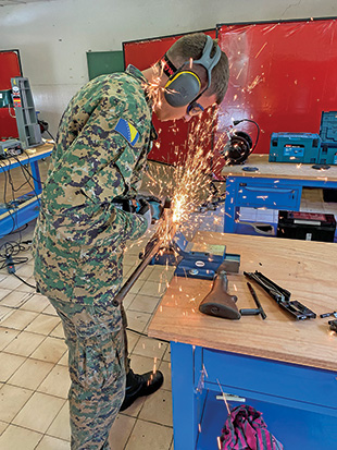 A man in a camouflage uniform destroys a machine gun by sawing it..