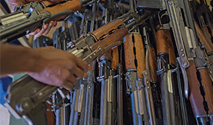 A hand picking up a rifle from a pile of other rifles.