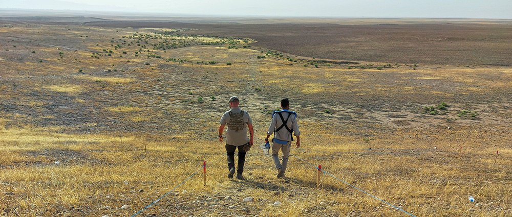 Two people walking down a hillside and along a path marked by tape.