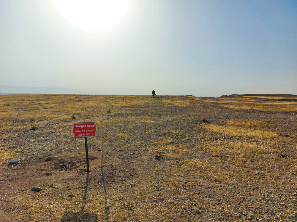 A single person on a hill, silhouetted against the horizon; in the foreground a red sign reads "Danger Area".
