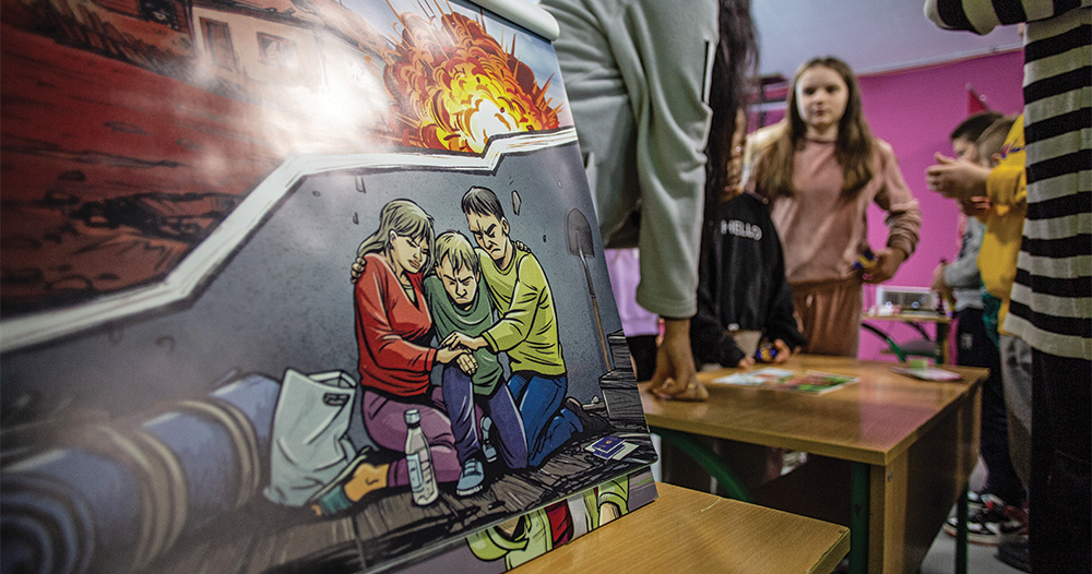 A drawing of a family sheltering from an explosion propped up on a table; children standing out-of-focus in the background