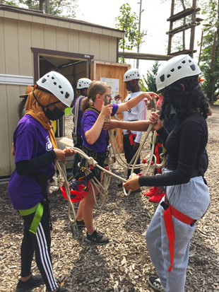 People wearing helmets but safety harnesses on preparing to climb a ropes course