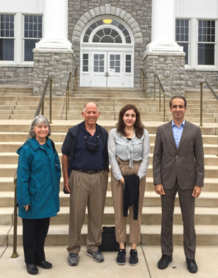 Four people stand in front of steps leading up to a large stone building.