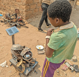 A boy looks at a pile of metal on a scale