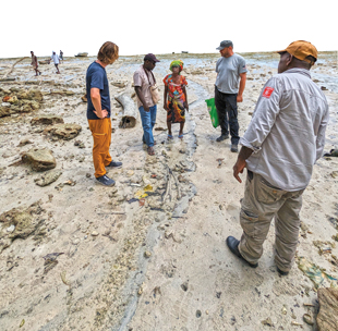 A groupe of people gather on a beach looking at a woman speaking.