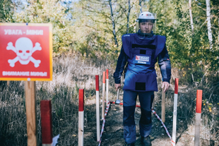 A person in blue protective clothing walks on a path by a sign that says Danger Mines