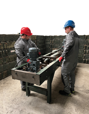 Two people wearing helmets stand on either side of a long table-like machine.