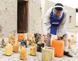 A person in protective gear leans over numerous plastic bottles that were once IEDs