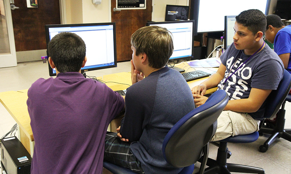 A CIS student volunteer helps two attendees with an assignment during CyberDay
