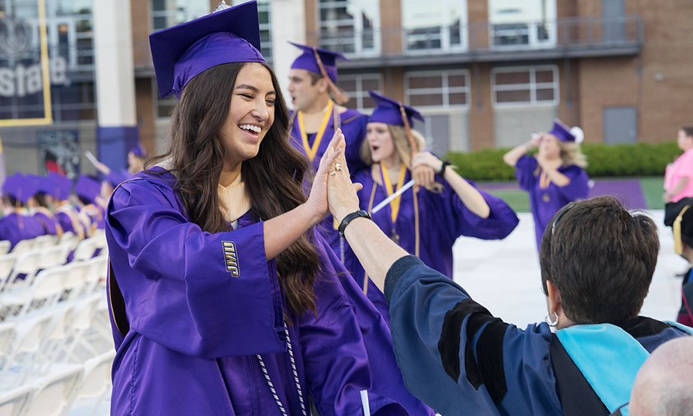 A female CoB graduate in cap and gown high fives a CoB professor - 2017