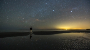 Garrett Martin on the beach at twilight underneath a starry sky