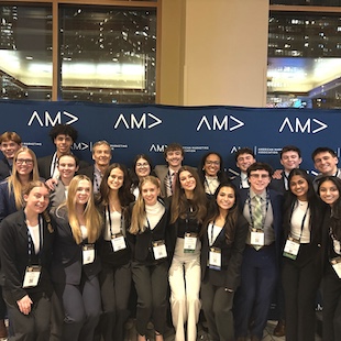 Group of conference attendees wearing name badges posing in front of an “AMA” branded backdrop.