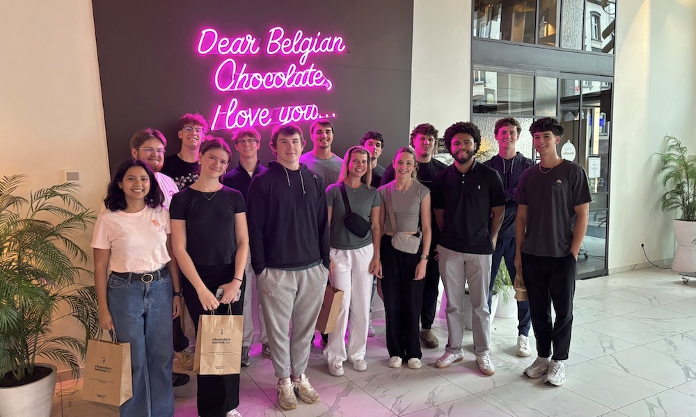 Group of students posing in front of a neon sign that reads "Dear Belgian Chocolate, Love you."