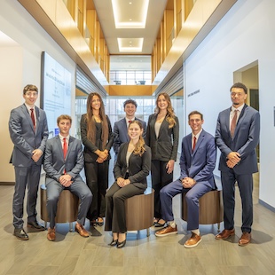 Group of professionally dressed students posing in a modern building lobby.