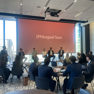 Panel discussion at a JPMorganChase event, with speakers seated on stage in front of a large JPMorganChase-branded screen and attendees listening at tables.