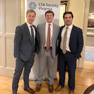Three men in business suits posing together at a CFA Society Virginia event, standing in front of a sign.