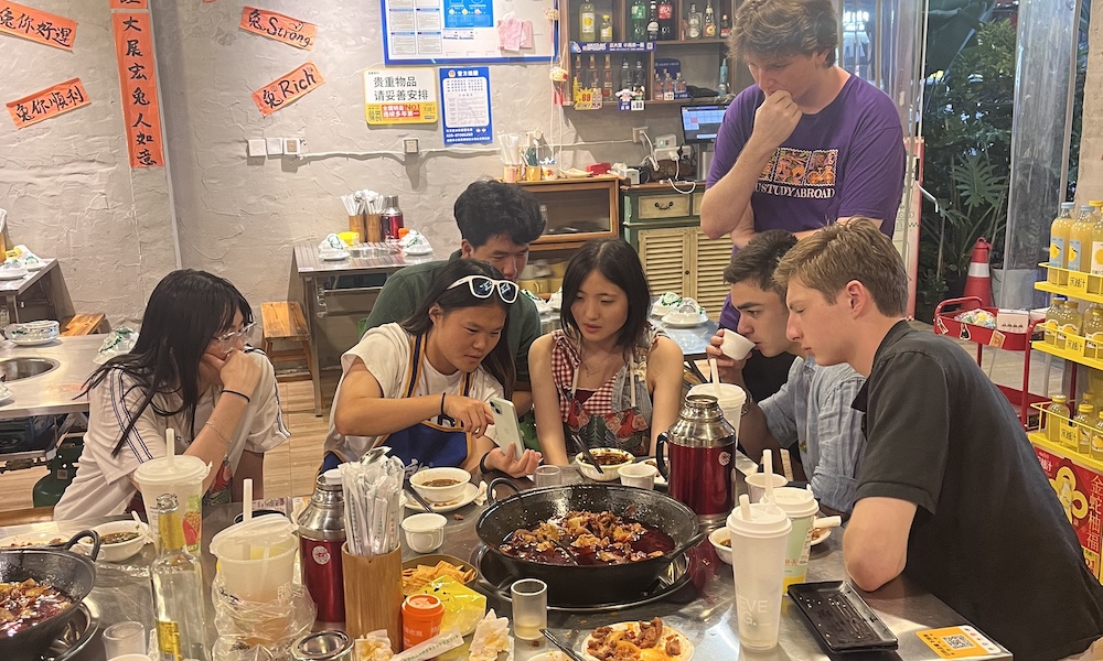 A group of friends gathered around a table, engaged in a lively conversation while sharing a hot pot meal in a casual dining setting.