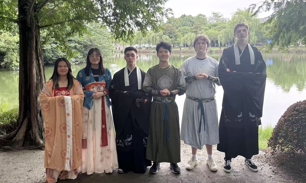 Group of six people in traditional Chinese clothing standing by a lake.