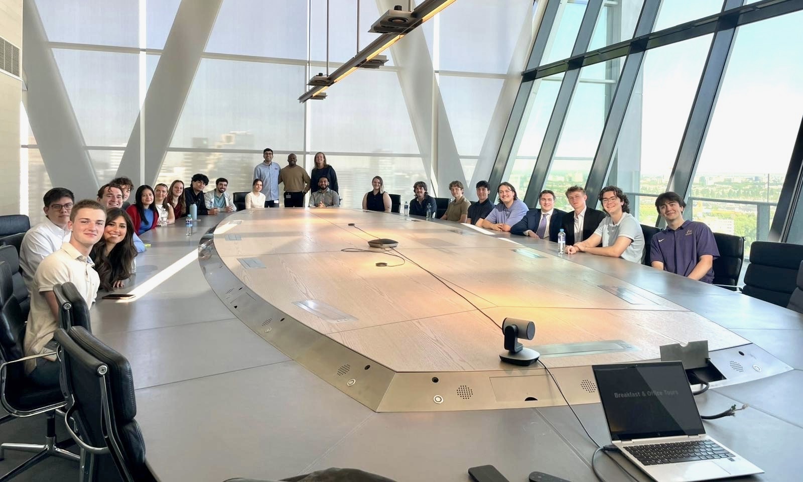 A group of students and mentors gathered around a large conference table at EY Amsterdam with a city view.