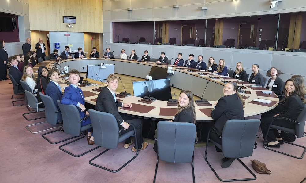 A group of students seated around a large conference table in a formal meeting setting at the European Commission.