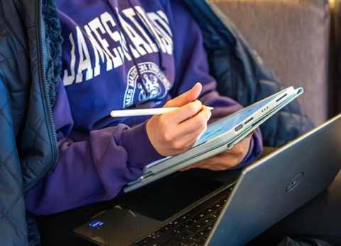 Close up picture of a student on their laptop wearing a JMU purple sweatshirt.