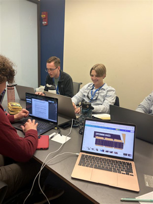 Four people working on laptops around a conference table in a meeting room.