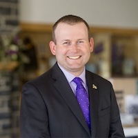 Eric Bowlin in a dark suit and purple tie in an indoor setting.