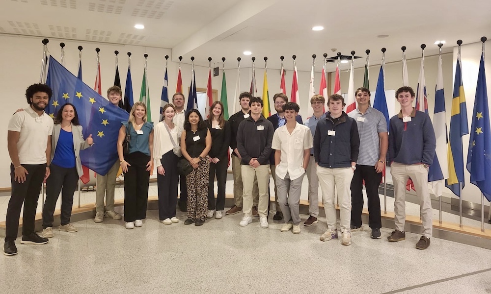 Group photo of students standing in front of various national flags, at the European Parliament..