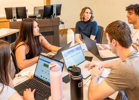 CoB Marketing students around a table in an office meeting room, using laptops and discussing real campaign strategies for the Dian Fossey Gorilla Fund.