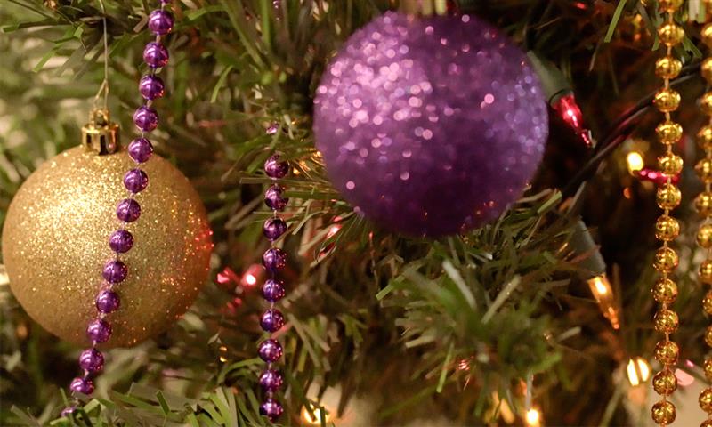 A close up images of purple and gold ornaments on a tree.