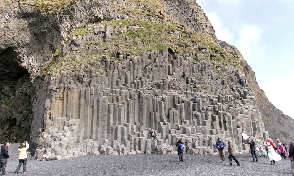 Spectacular hexagonal basalt columns at Reynisfjara Beach in Iceland, with visitors exploring the unique geological formation.