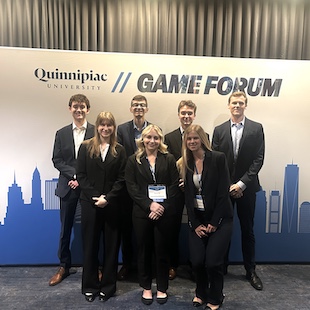 Group of students in business attire posing at the Quinnipiac University GAME Forum event backdrop.