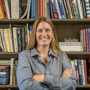 Nicole Wright with arms crossed standing in front of a bookshelf filled with books.