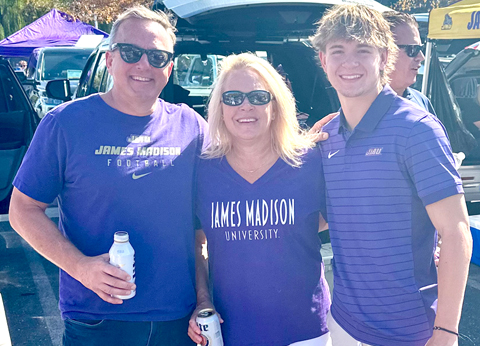 The Rennyson family wearing James Madison University shirts smile at a tailgate in a parking lot.