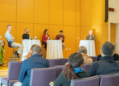 Teaching Academy event with panel discussion in a lecture hall, with participants seated at tables facing an audience.