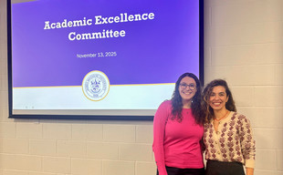 Two women smiling and posing in front of a presentation slide titled "Academic Excellence Committee" dated November 13, 2025.