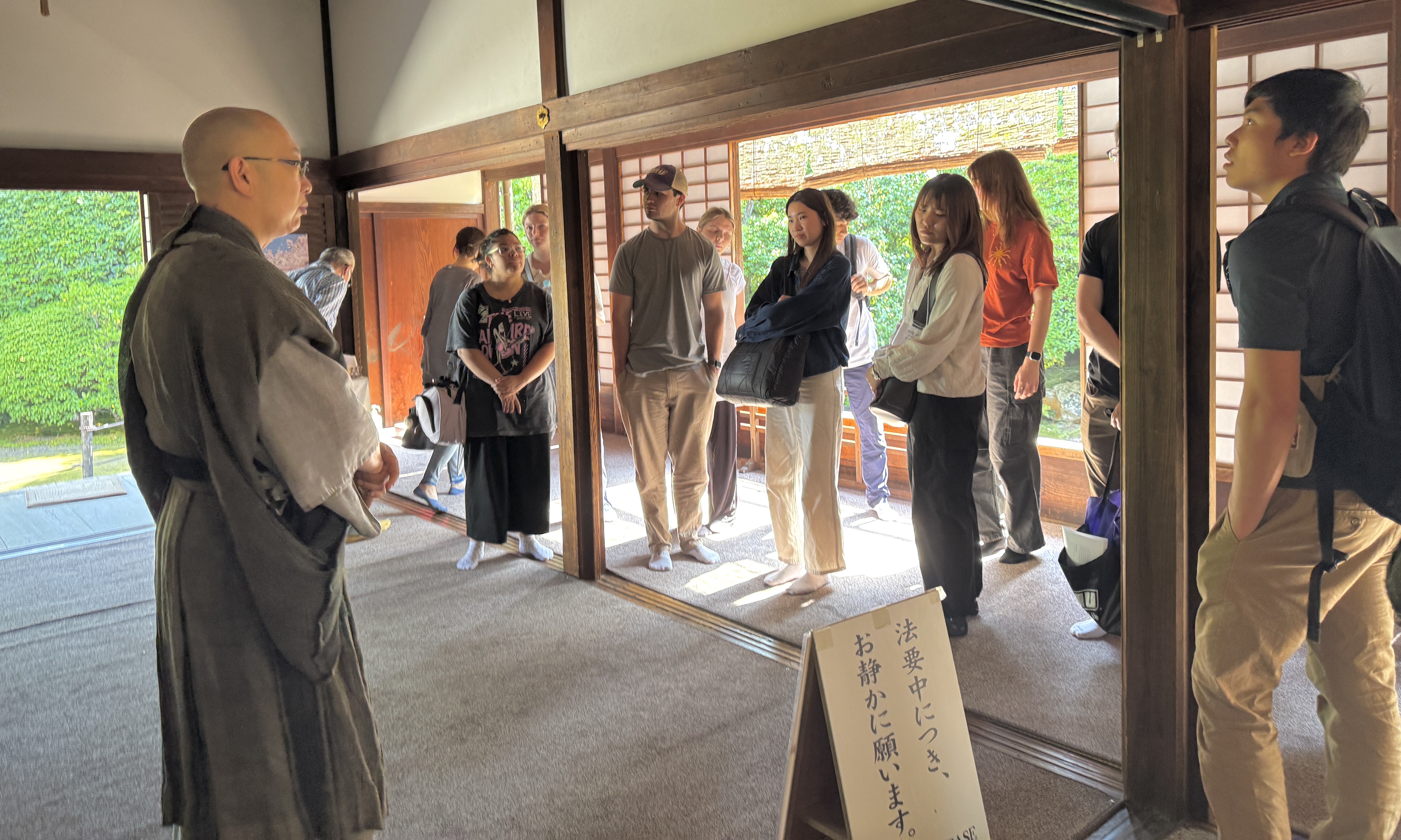 A monk addresses a group of visitors in a traditional Japanese temple, emphasizing the serene atmosphere and cultural experience.