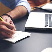 image of someone working on a computer and taking notes.