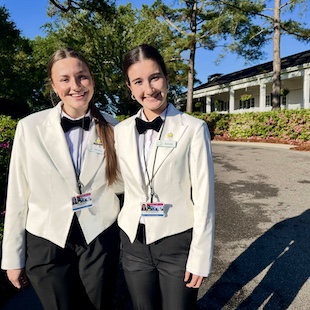 Rachel Bailey (left) and Rachel Connolly (right) dressed in white and black tuxedos while the act as servers.