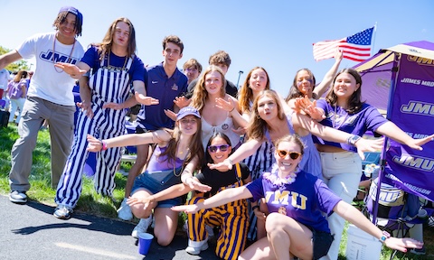 Students making hand motions for chant JMU Duuuukes at a football tailgate