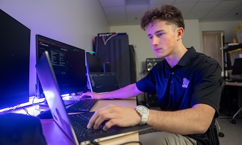 Will Jedrzejczak working at a computer in a black JMU polo shirt
